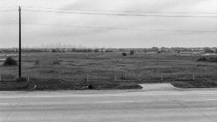 Open grassland behind a new curb cut and a power line, the city skyline faint on the horizon