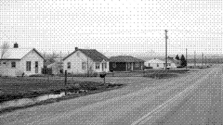 Small houses on a rural road with a city skyline on the horizon
